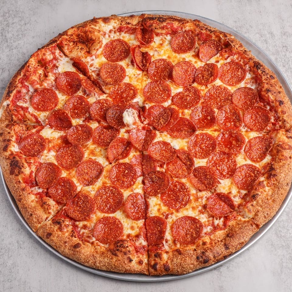 Large pepperoni pizza with melted cheese and a golden crust, sliced on a round metal tray.